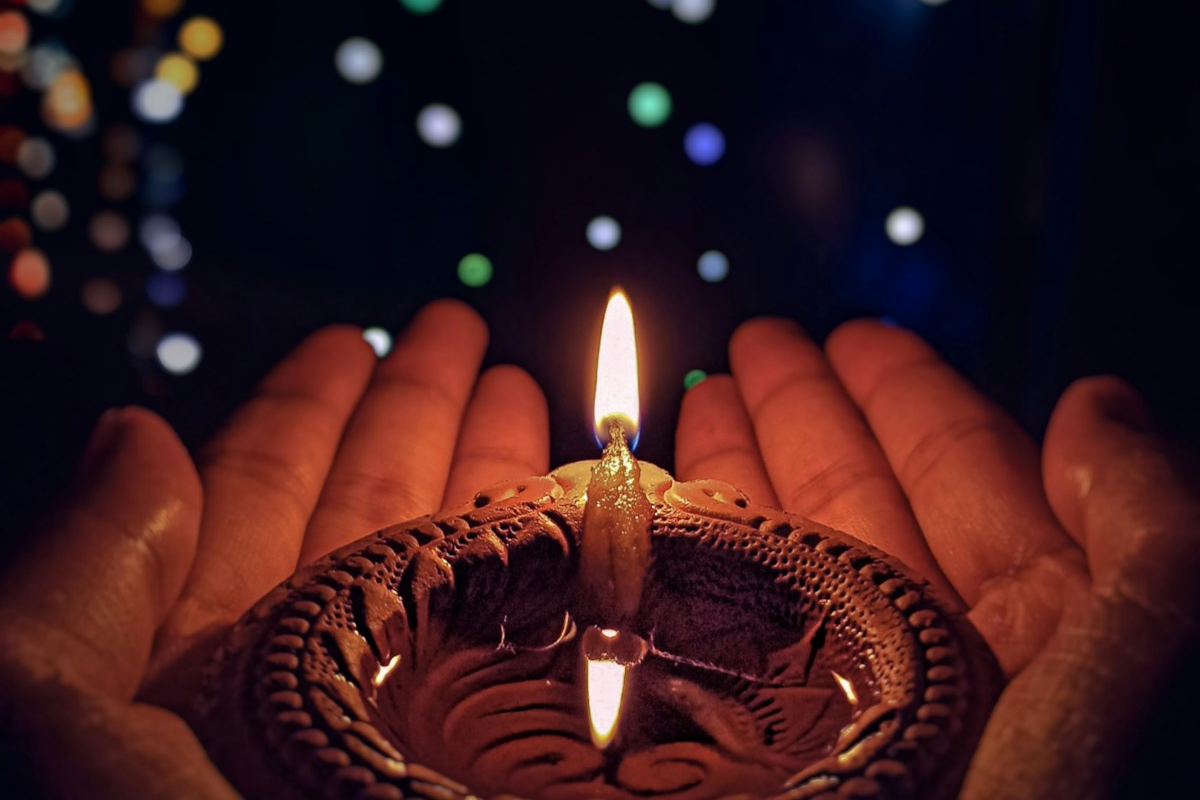Hands holding a lit clay lamp in the dark