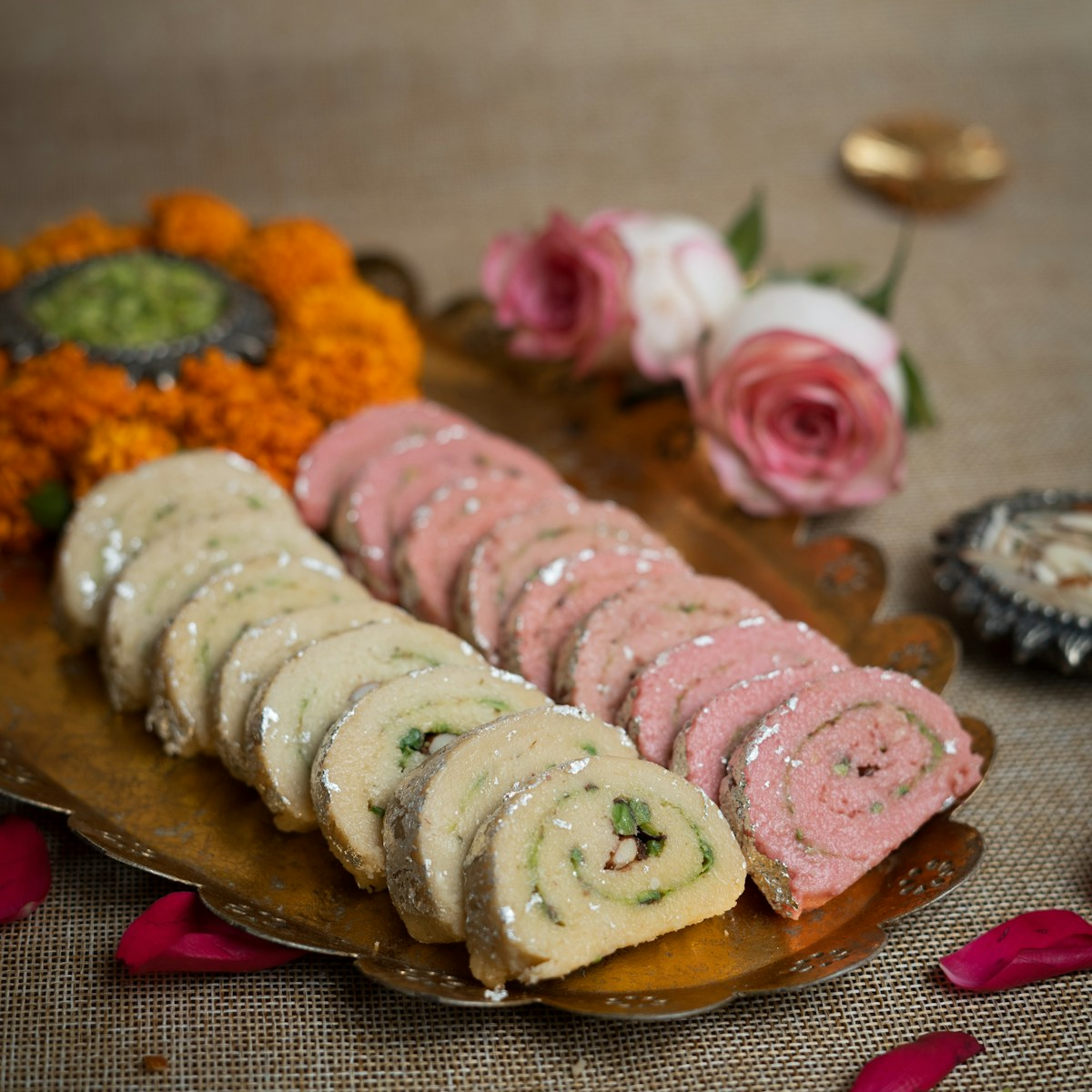 Rolled Bengali sweets arranged on a brass tray with marigolds